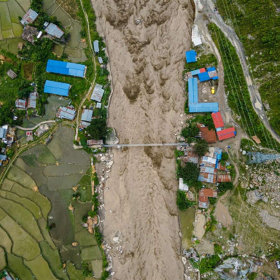 Aerial view of floodwater passing homes and fields in Rasuwa